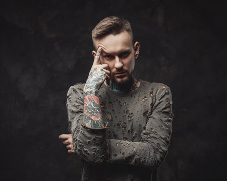 Dressed in ragged shirt stylish and bearded hipster with modern haircut poses in dark backgroundの写真素材