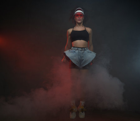 Beautiful female dancer in short cloth ing with red cap jumps in dark background posing in air.の写真素材