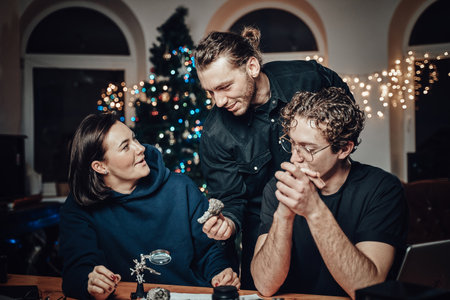 Positive company of a woman and two guys sit at table there a magnifier and some other tools and...