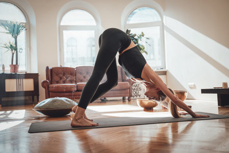 Warm and tranquil living room with sunshine and simple design in daytime and concentrated woman does yoga in pilates pose on mat.の写真素材