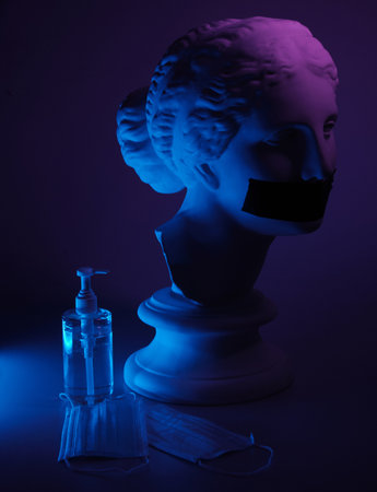 Greek female bust with taped mouth and protective facial masks with antiseptic in darkness and colourful light.の写真素材