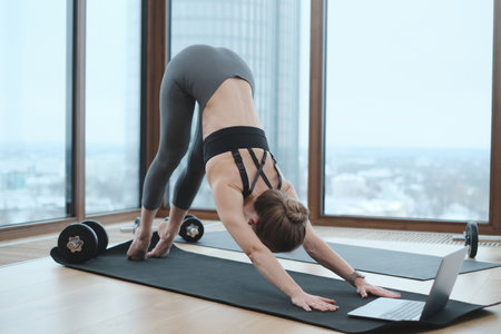 Portrait of a flexible and graceful female person in sportive clothing doing yoga on mat using a...