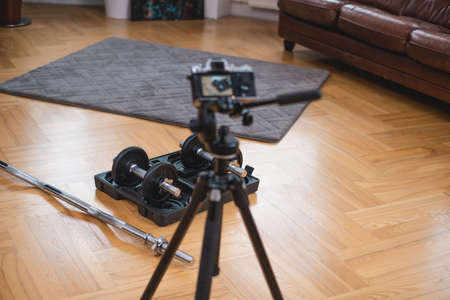 Professional photocamera shoots dumbells and barbell with box they are on floor in living room.の写真素材