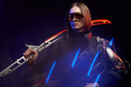 Serious military woman in stylish dark clothing and with implant on her shoulder poses in dark...
