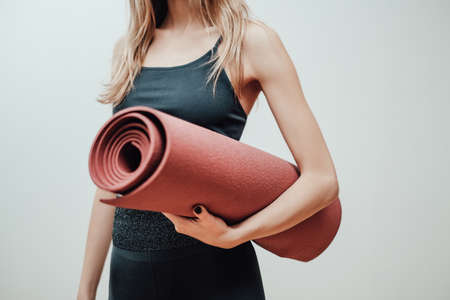 Young female athlete in black sportswear poses in white background holding a mat.の写真素材