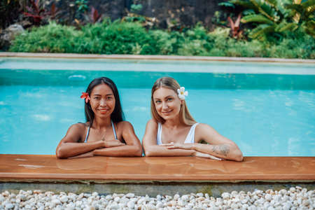 Positive portrait of happy women they are swimming in pool with clear blue water and look at camera smiling.の写真素材