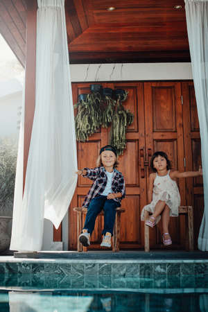 Portrait of playful preschool boy and girl which sit on chairs near door and swimming pool holding curtains.の写真素材