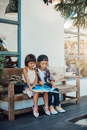 Portrait of youth and cute children they are reading scientic book sitting on a becnh in park in daytime.の写真素材