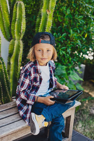 Portrait of cheerful and young boy which poses on bench holding a tablet and looking at camera.の写真素材