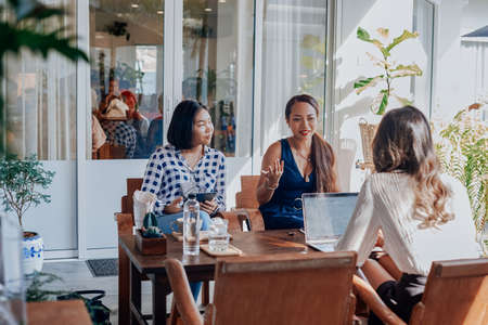 Female team of asian women sit at table together and planning their prohect using a laptop in comfortable office in daytime.の写真素材