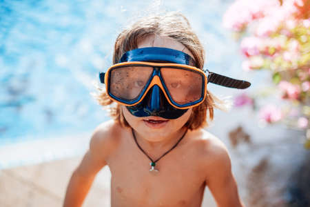 Swimming and enjoynment. Cheerful kid with naked body weared with goggles looks at camera in background of shorescape.の写真素材