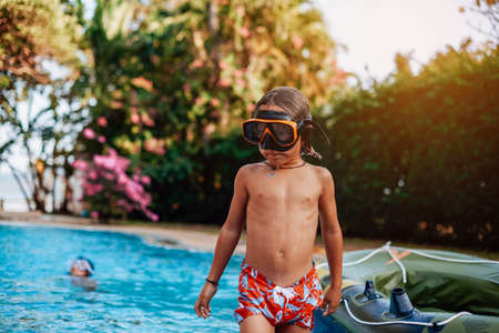Youth boy in swimwear weared with goggles swim in a pool with his little friends on inflatable boat.の写真素材