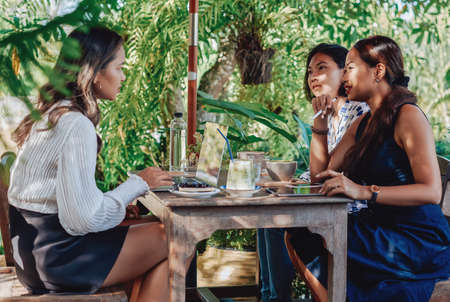 Asian female coworkers at meeting discuss their project sitting at table outside and using a laptop with tablet in daytime.の写真素材