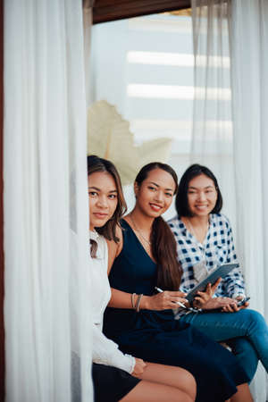 Creative work of female designers. Three asian girls in formal clothing pose on doorstep looking at camera and smiling.の写真素材