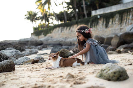 Warm photography of a cute dog and preteen girl in dress with wreath they are playing on seacoast in thailnd.の写真素材