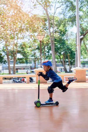 Protected with sports equipment preschool kid rides scooter through the road enjoying his holidays. Extreme sports and little boy.の写真素材