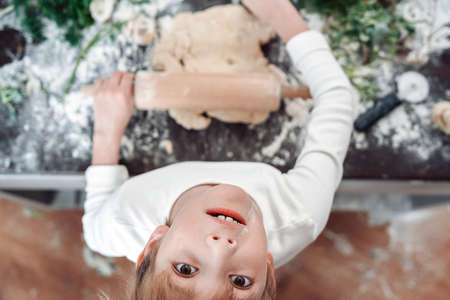 Portrait of a young and astonished boy in white shirts he looks at camera and rolls a dough...