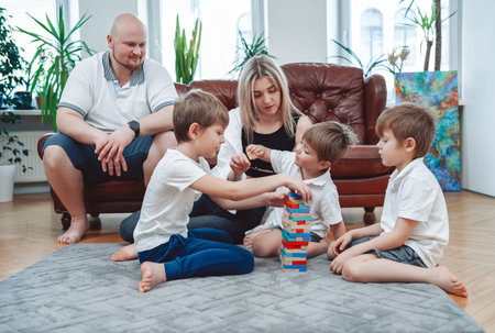Warm portrait of joyful family of mother and father with their children they play tower challenge...