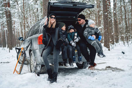 Cheerful family of father and mother with their children on their vacations with car in winter wood.の写真素材