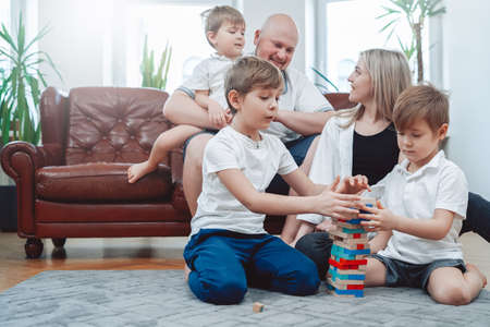 Warm portrait of joyful family of mother and father with their children they play tower challenge...