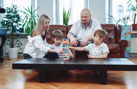 Couple of caucasian man and woman constructing a tower from bricks with their two little boys in modern living room.の写真素材