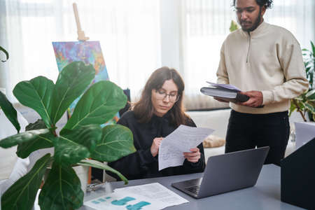 Friendly portrait of a bearded indian man and young caucasian woman their do their work in design studio in daytime.の写真素材