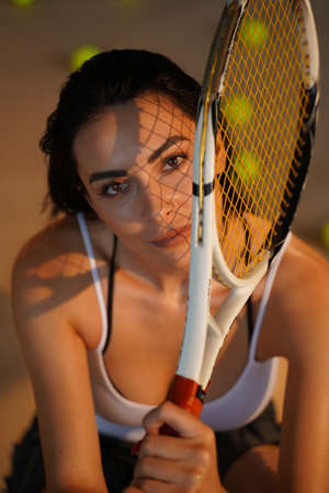 Close up portrait of pretty tennis player holding racket looking at camera with sunlight and shadows.の写真素材