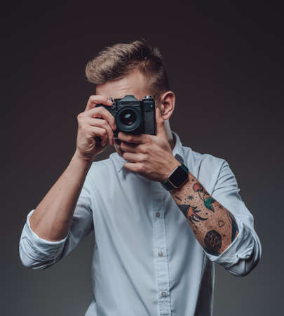 Stylish photographer with tattooed hand does shot using his photo camera. Professional portrait of a young man.の写真素材