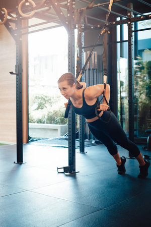 Modern gym with different training apparatus in daytime. Female fitness person does physical...
