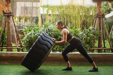 Special training and concept of a sportswoman doing hard workout. Female athlete pushing a huge wheel outside in Thailand.の写真素材