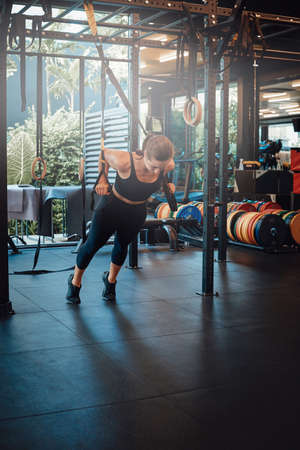 Modern gym with different training apparatus in daytime. Female fitness person does physical exercise balancing and relaxing.の写真素材