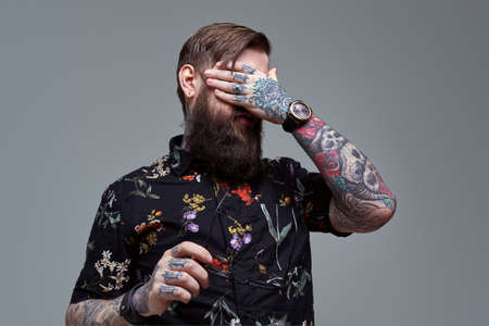 Portrait of a tired man with tattoos wearing stylish clothing with watch in gray background. Handsome guy in retro style.の写真素材