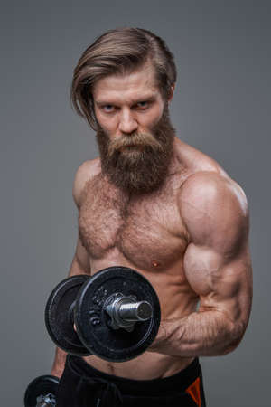Handsome bodybuilder poses in gray background holding dumbellsの写真素材
