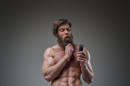 Pensive bodybuilder holding hair clipper in gray background