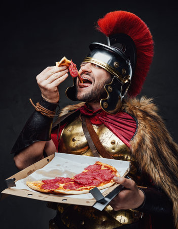 Antique legionary eats pizza against dark backgroundの写真素材