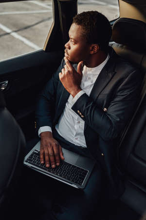 Pensive black employee working on laptop inside of carの写真素材