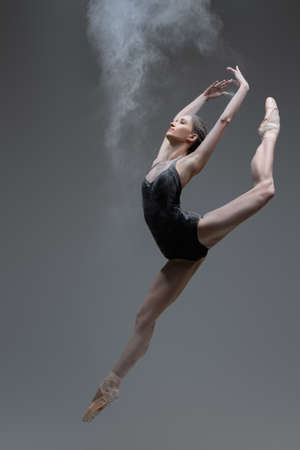 Skilled ballerina dancing leaping against gray backgroundの写真素材