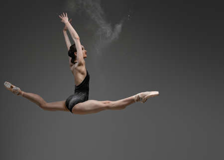 Leaping woman with raised arms against gray backgroundの写真素材