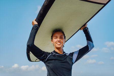 Cheerful woman in wetsuit holding surfboard on beachの写真素材