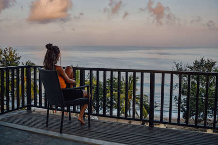 Carefree woman sitting on chair against beach landscapeの写真素材