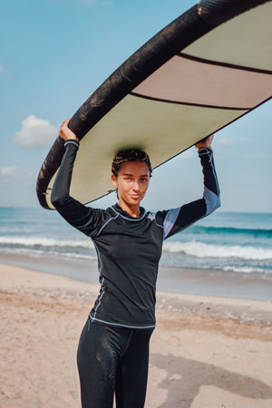 Cheerful woman in wetsuit holding surfboard on beachの写真素材