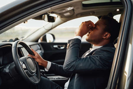 Exhausted african businessperson sitting inside of car holding wheel.の写真素材