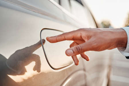 Shot of businessman with his finger on fuel tank of car