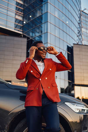 Cheerful african businessperson with phone and car outsideの写真素材