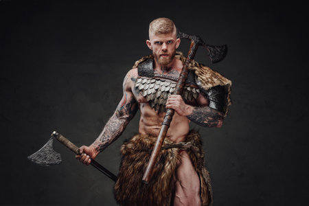 Strong tattooed warrior in light armour and fur with two axes in dark