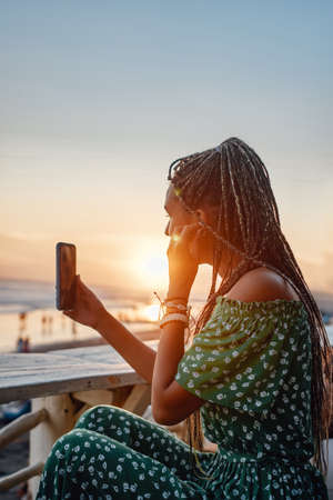 Woman with dreadlocks on beach with earphones and phone