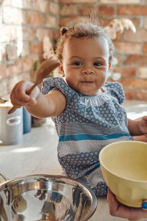 Little girl with wooden spoon on kitchen in daytimeの写真素材