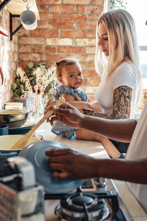 Cheerful little girl with her parents cooking some food on kitchenの写真素材