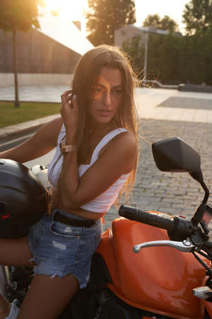 Stylish woman biker posing on motorcycle against cityscape
