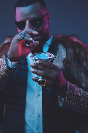 Joyful african businessman with diamond and fur coatの写真素材